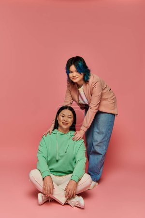 A mother and her teenage daughter are posing together in front of a vibrant pink background in a studio setting.
