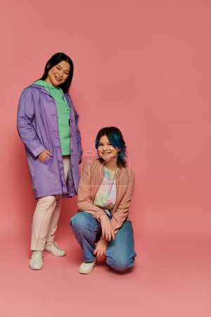 Asian mother and her teenage daughter posing confidently in front of a pink background in a stylish studio setting.