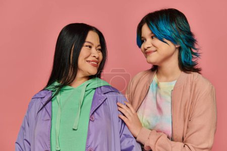 Téléchargez les photos : Mère asiatique et fille adolescente debout ensemble en tenue décontractée devant un fond rose vibrant. - en image libre de droit