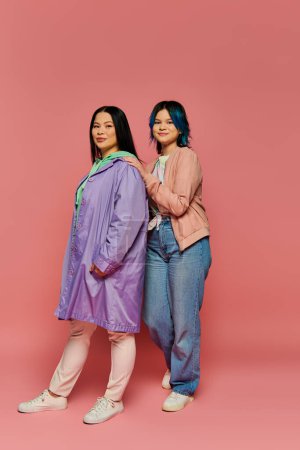 Photo for Asian mother and teenage daughter stand together, exuding love and empowerment in front of a vibrant pink backdrop. - Royalty Free Image