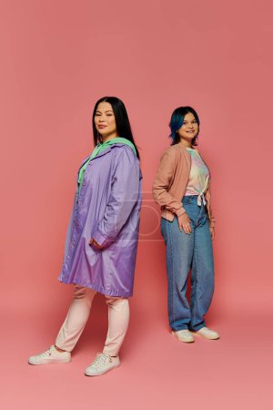 Photo for An Asian mother and her teenage daughter stand next to each other in casual wear against a pink background. - Royalty Free Image