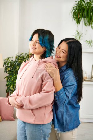 Foto de Una madre asiática y su hija adolescente están lado a lado en una acogedora sala de estar, compartiendo un momento de conexión y calidez. - Imagen libre de derechos
