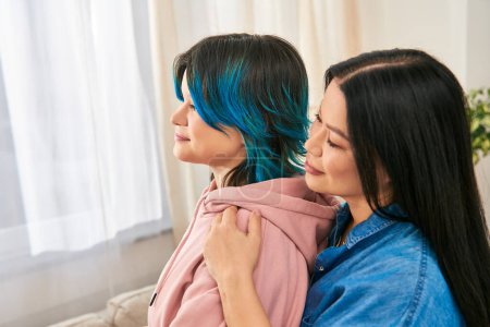 Photo for A mother and teenage daughter, of Asian descent, stand closely together in casual attire, sharing a moment of connection at home. - Royalty Free Image