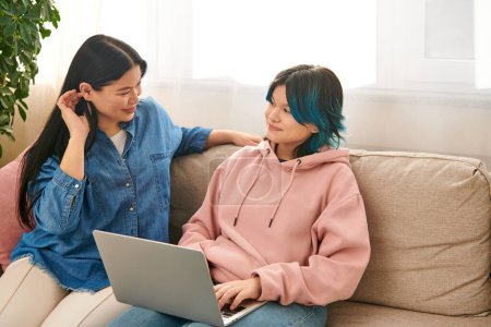 Téléchargez les photos : Une mère asiatique et sa fille adolescente, en tenue décontractée, s'assoient sur un canapé, absorbés alors qu'ils regardent tous deux un écran d'ordinateur portable. - en image libre de droit