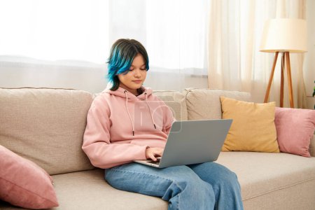 Téléchargez les photos : Adolescent fille avec les cheveux bleus se trouve sur le canapé en utilisant un ordinateur portable. - en image libre de droit