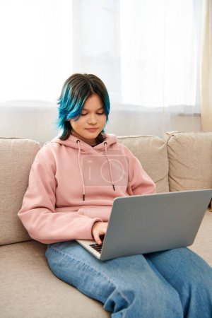An Asian girl with blue hair sits on a couch, typing on a laptop, while spending time at home.