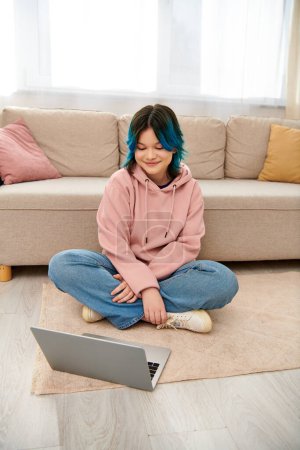 Téléchargez les photos : Une adolescente asiatique assise sur le sol, absorbée par un ordinateur portable - en image libre de droit