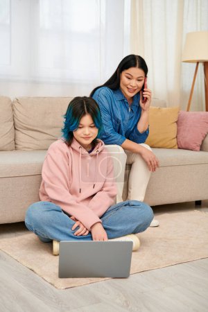Photo for An Asian mother and her teenage daughter in casual wear sit together on the floor, sharing a quiet moment of connection. - Royalty Free Image
