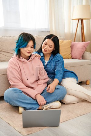 Téléchargez les photos : Deux femmes, une mère asiatique et sa fille adolescente, s'assoient par terre à l'aide d'un ordinateur portable ensemble. - en image libre de droit