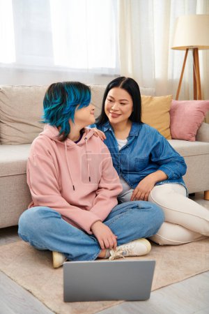 Photo for An Asian mother and her teenage daughter sit on the floor, engrossed in a laptop screen, spending quality time together at home. - Royalty Free Image