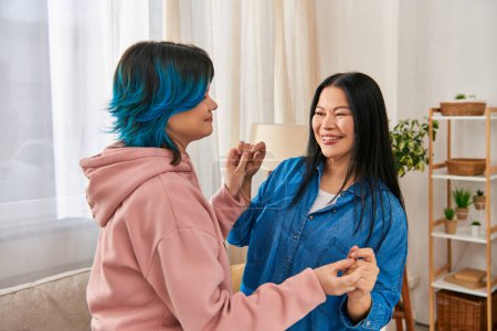 An Asian mother and her teenage daughter stand together in a cozy living room, sharing a moment of closeness and connection.