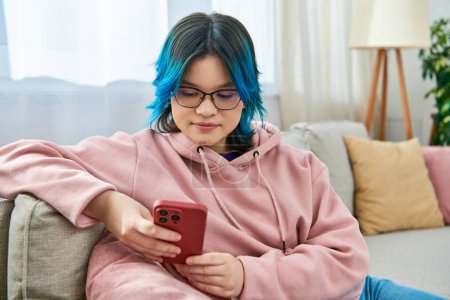 Asian girl with blue hair sits contentedly on a couch in casual wear at home.