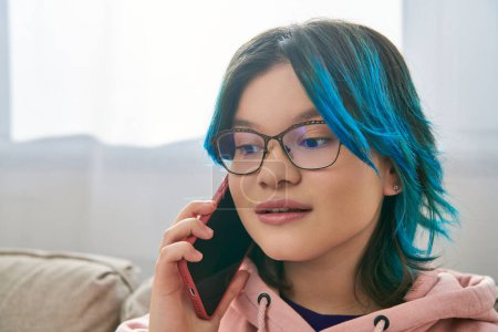 An Asian girl with vibrant blue hair engages in a phone conversation while spending time at home.