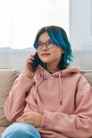 Ein Teenager-Mädchen sitzt auf einer Couch und unterhält sich über ein Mobiltelefon.