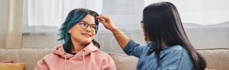 Photo for A mother with unique blue hair is tenderly combing her teenage daughters hair at home in a heartwarming moment of bonding. - Royalty Free Image