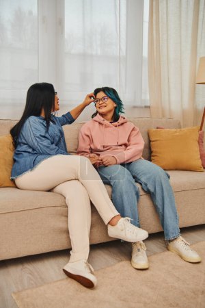 Téléchargez les photos : Asian mother and daughter in casual attire engaged in a lively conversation while sitting on a cozy couch at home. - en image libre de droit