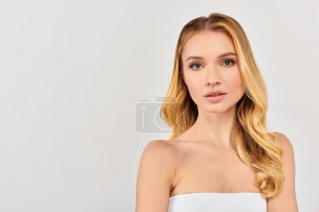 Téléchargez les photos : Une jeune femme aux longs cheveux blonds pose gracieusement sur un fond blanc. - en image libre de droit