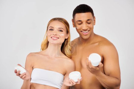 Trendy couple holding creams together during skin care routine.
