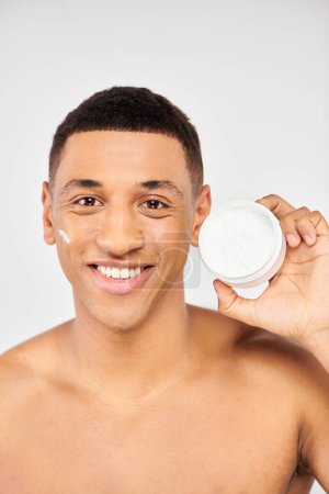 Téléchargez les photos : A young man holds a container of facial cream. - en image libre de droit