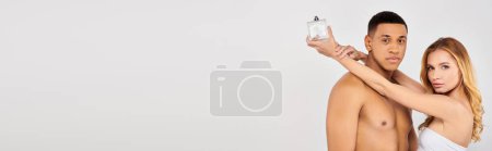 A diverse couple poses gracefully against a white backdrop, parfume.