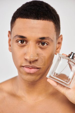 Junger Mann hält selbstbewusst eine Flasche Parfüm in der Hand.