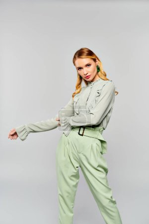 Stylish woman in green outfit striking a pose on gray backdrop.