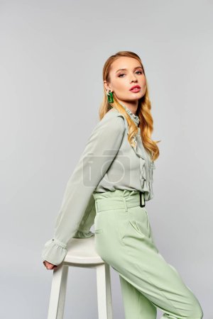Woman in a green blouse posing gracefully on a stool.