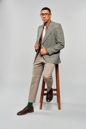 Homme assis élégamment sur tabouret dans un élégant blazer à carreaux.
