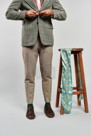 Stilvoller Mann in Blazer und Krawatte anmutig auf einem Hocker stehend.