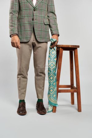 Téléchargez les photos : Homme élégant en plaid blazer et cravate se tient avec confiance sur un tabouret. - en image libre de droit