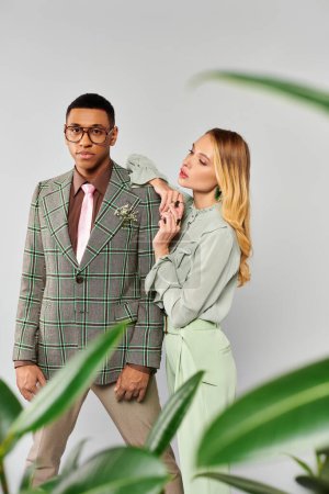 Man and woman romantically pose in front of a vibrant green plant.