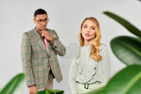 Foto de Un hombre y una mujer elegantemente de pie junto a una planta, admirando su belleza. - Imagen libre de derechos