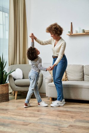 A happy African American mother and daughter dancing together in their cozy living room, sharing special moments and creating lasting memories.