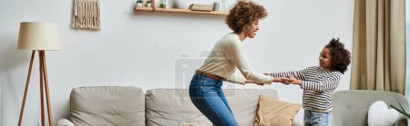 An African American mother and daughter gleefully dance together on a couch, enjoying quality time at home.
