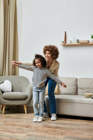 Téléchargez les photos : An African American mother and daughter happily dancing together in their cozy living room. - en image libre de droit