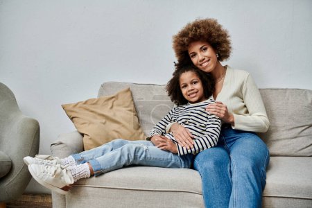Happy African American mother and daughter spending quality time together, sitting comfortably on a couch.