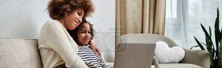 Téléchargez les photos : Une heureuse mère et fille afro-américaine assise sur un canapé, s'engageant avec un ordinateur portable ensemble. - en image libre de droit