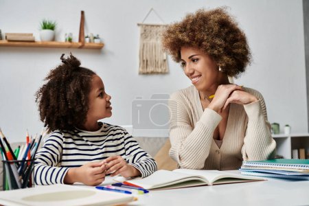 An African American mother and young daughter sit at a desk, engaged in learning and bonding in their home.