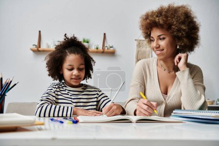 Happy African American mother and daughter sharing a moment, writing in a notebook at home.