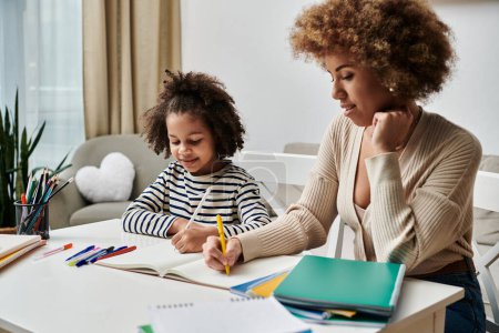 Photo for A happy African American mother and daughter focus on their homework together at home. - Royalty Free Image