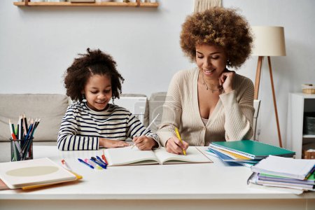 Eine afroamerikanische Mutter und ihre Tochter sitzen an einem Tisch, vertieft in die gemeinsamen Hausaufgaben und teilen einen besonderen Moment.