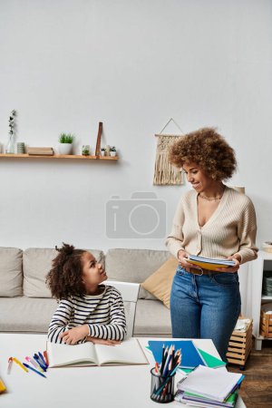 Una alegre mujer afroamericana y su hija se sientan en una mesa, compartiendo un momento precioso en su cálida y acogedora sala de estar.