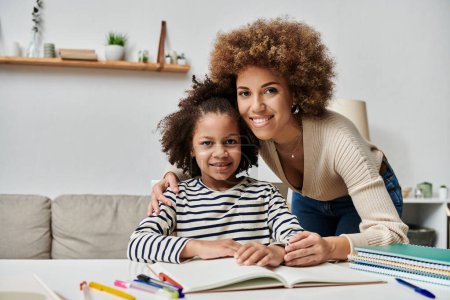 Téléchargez les photos : A happy African American mother and her daughter sit together at a table, enjoying quality time at home. - en image libre de droit
