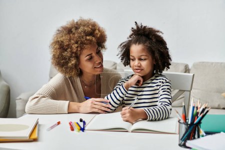 A joyful African American mother assists her daughter with homework, fostering a strong bond through quality time spent together at home.