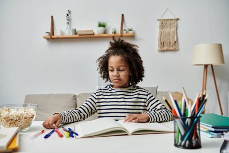 Una niña de ascendencia afroamericana se sienta en una mesa con un libro y lápices de colores