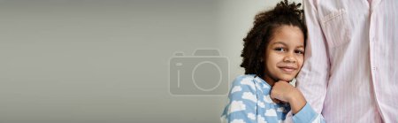 Téléchargez les photos : Un homme afro-américain et sa petite fille en pyjama frappant une pose ensemble, rayonnant de bonheur et d'amour sur un fond gris. - en image libre de droit