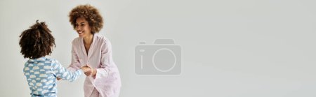 Téléchargez les photos : Une heureuse mère et fille afro-américaine en pyjama dansant sur fond blanc. - en image libre de droit