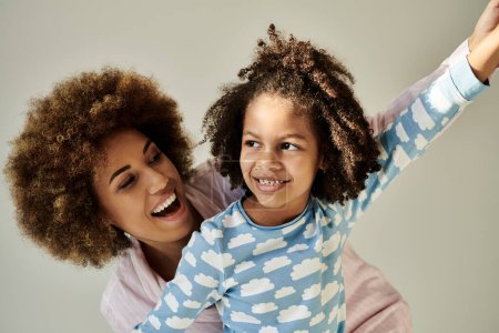 Happy African American mother and daughter in pajamas, enjoying quality time together on a grey background.