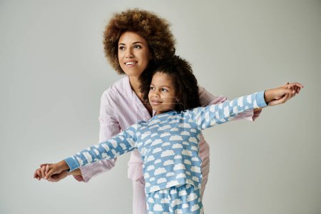 Téléchargez les photos : A happy African American mother and daughter in pajamas striking a pose on a grey background. - en image libre de droit