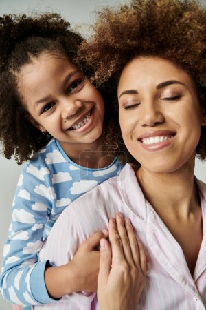 Photo for An African American mother and daughter in pajamas smiling happily together against a grey background. - Royalty Free Image